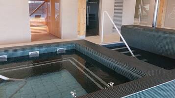A spa area with a tiled hot tub, a wooden bench, and a shower area.