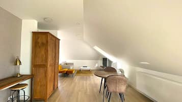 A spacious loft with a high ceiling, wooden flooring, a dining area with a table and chairs, a sofa, and a wooden cabinet.
