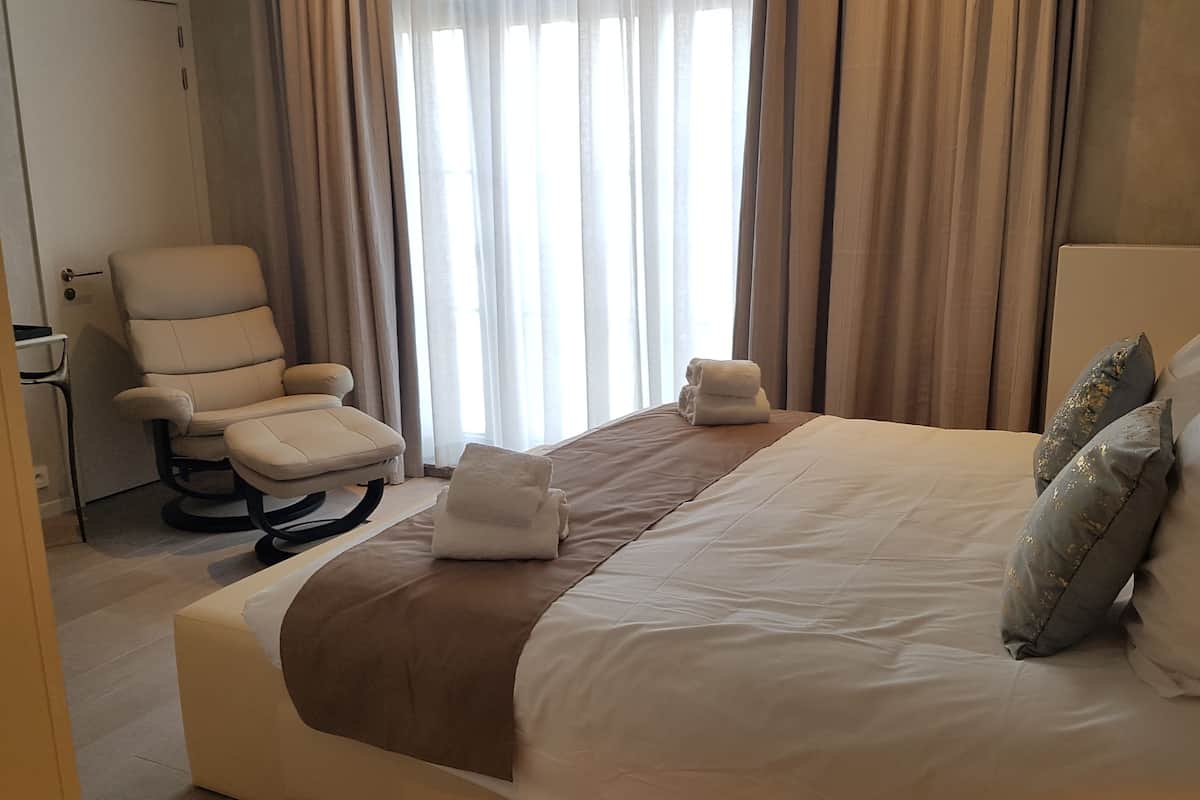 Quarto de hotel com cama, poltrona e janela com cortinas.