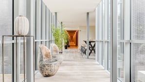 Un interior moderno con un largo pasillo, paredes de vidrio y zonas de estar con plantas.