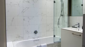 Een moderne badkamer met een douchecabine van glas, een witte badkuip en een wastafel met spiegel.