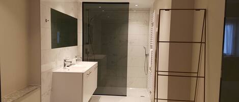 A modern bathroom with a glass shower enclosure, a white vanity with a mirror, and a towel rack.