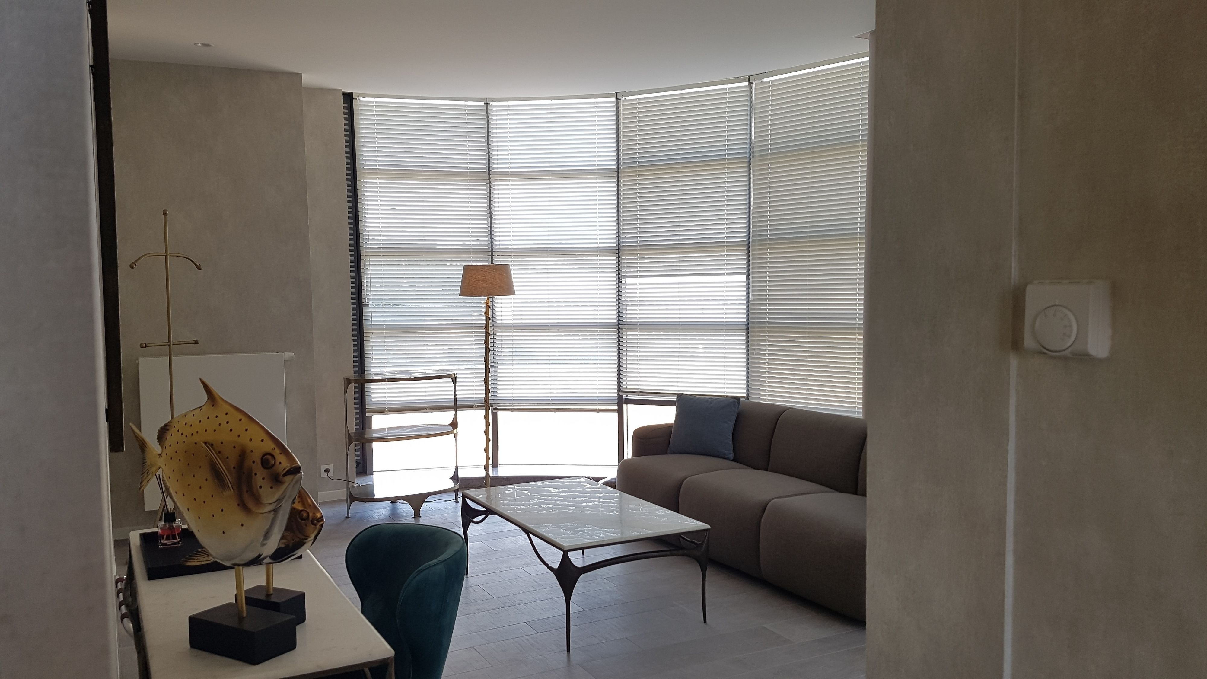 Uma sala de estar moderna com um sofá, uma mesa de centro e uma escultura de peixe sobre uma mesinha lateral.