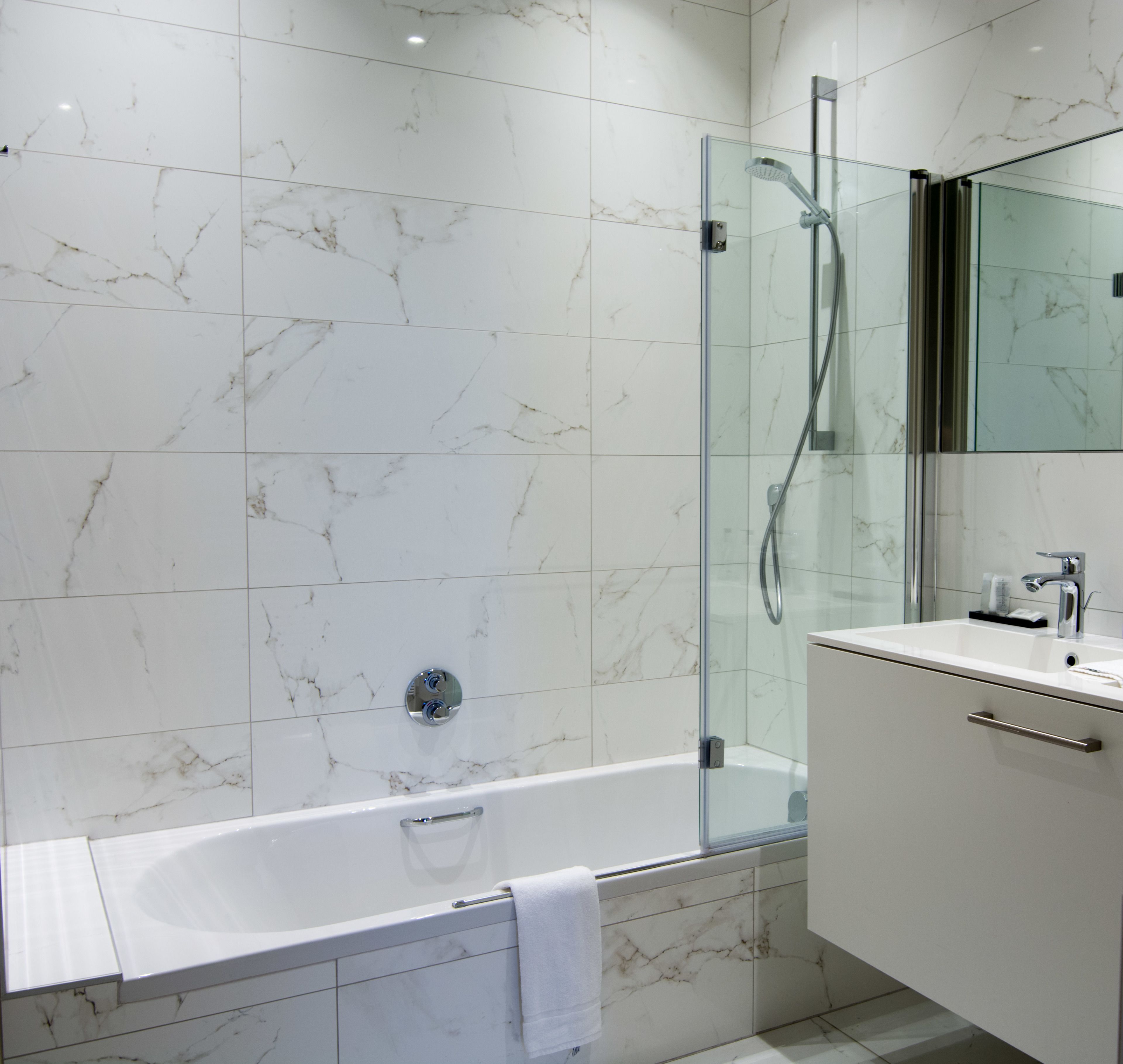 Un baño moderno con ducha envuelta en vidrio, una bañera blanca y un tocador con espejo.