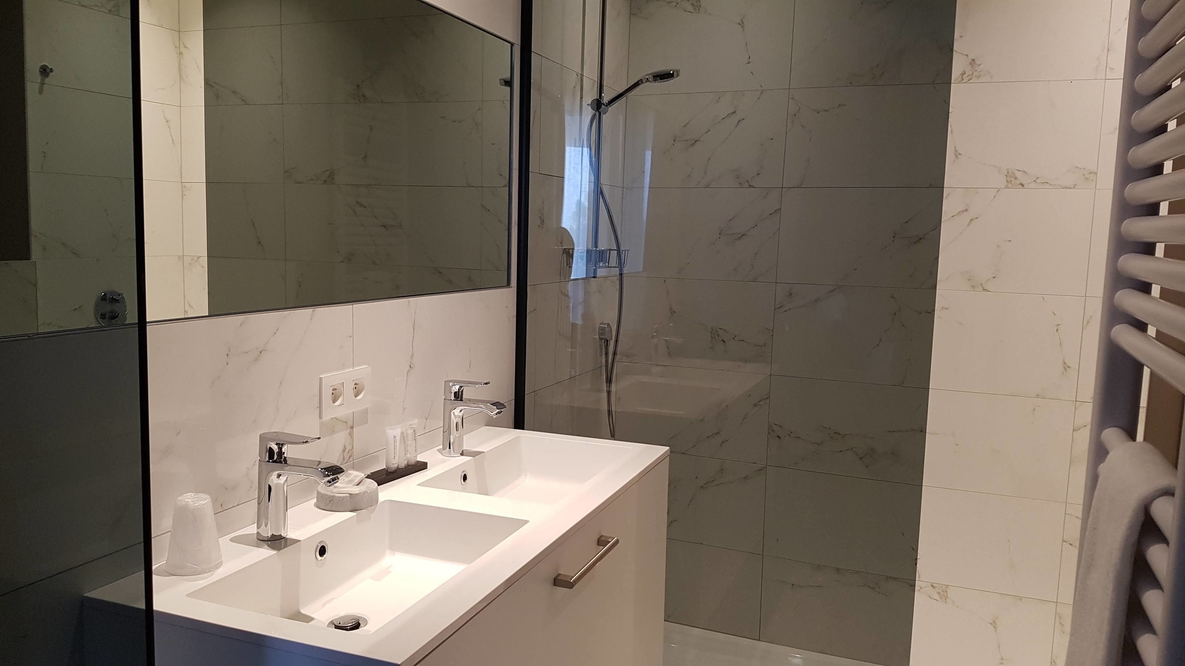 A modern bathroom with a large mirror, a white sink, and a glass-enclosed shower area.