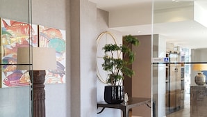 Zona de recepción con separador de vidrio, suelo de madera, planta en maceta y mostrador de recepción.