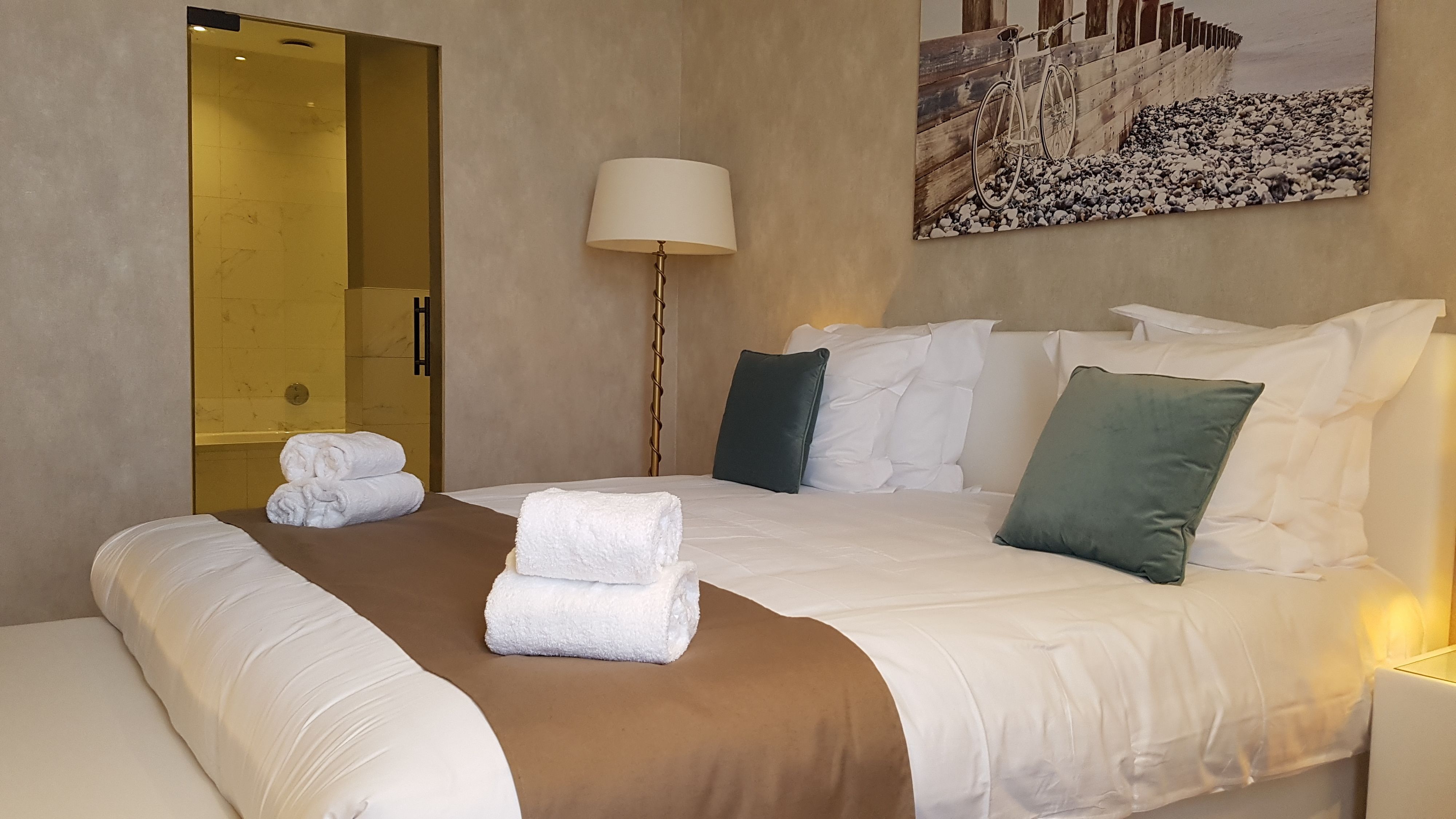 A hotel room with a bed, towels, a lamp, and a painting on the wall.