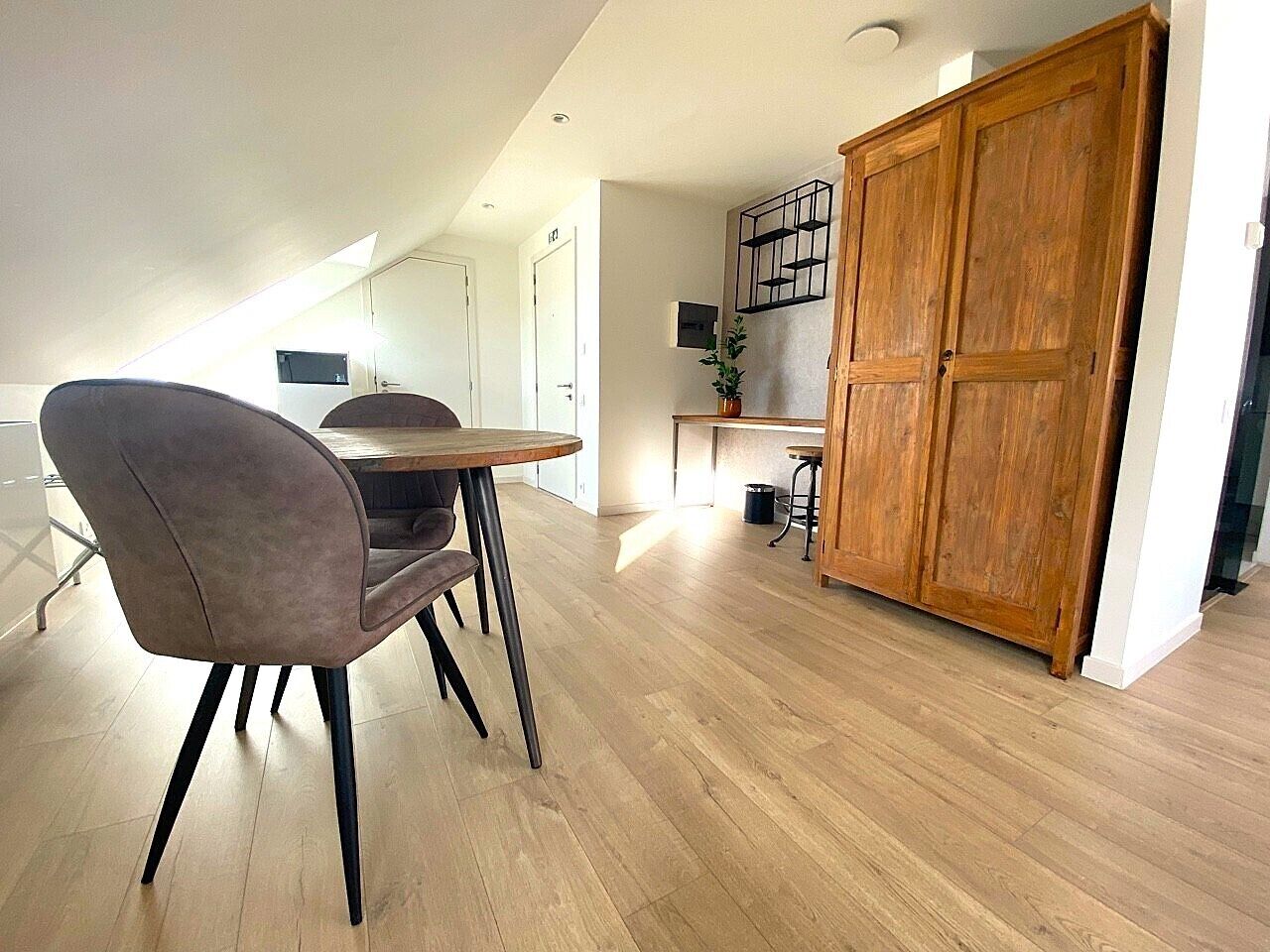 A modern kitchen with wooden flooring, a dining area with a table and chairs, and a large wooden wardrobe.