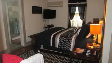 A hotel room with a bed, a desk with a lamp, a TV on the wall, and a window with curtains.