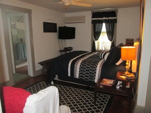 A hotel room with a bed, a desk with a lamp, a TV on the wall, and a window with curtains. - Buck's Homestead B&B (Montgomery)