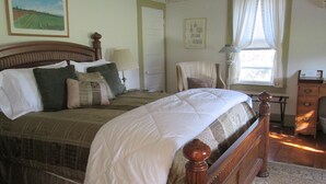 A neatly made bed with a wooden headboard, a bedside table with a lamp, and a window with curtains. - Buck's Homestead B&B (Montgomery)
