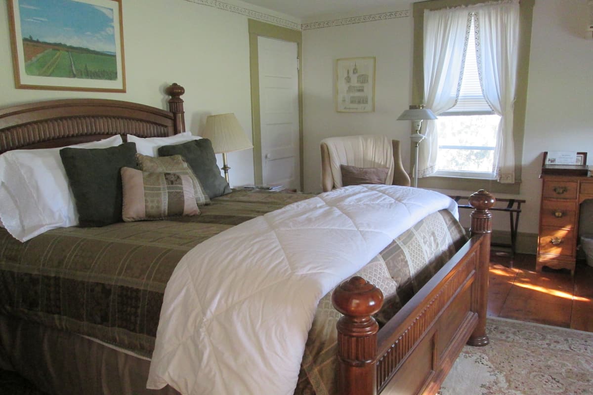 A neatly made bed with a wooden headboard, a bedside table with a lamp, and a window with curtains.