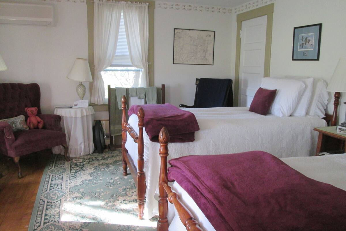 A bedroom with two beds, a chair, a table, and a window with curtains.