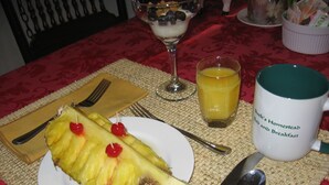 A table with a plate of pineapple, a glass of orange juice, a mug, and cutlery. - Buck's Homestead B&B (Montgomery)