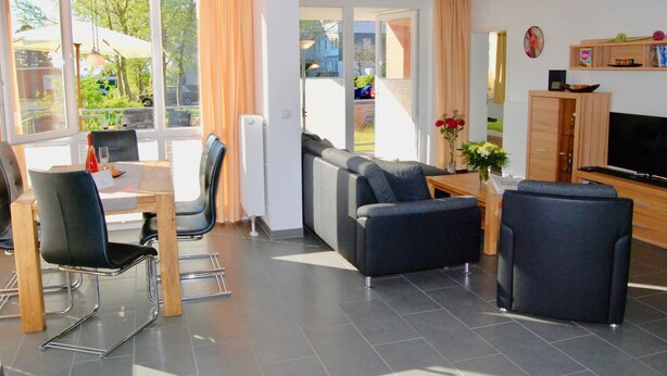 A modern living room with a sofa, chairs, a TV, and a dining area with a table and chairs. - Leuchtturm 4 (Grossenbrode)