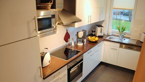 A modern kitchen with white cabinets, stainless steel appliances, a built-in oven, and a window with a view of the outdoors. - Leuchtturm 4 (Grossenbrode)