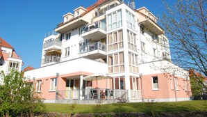 A multi-story hotel with balconies, a covered outdoor seating area, and a well-maintained lawn. - Leuchtturm 4 (Grossenbrode)