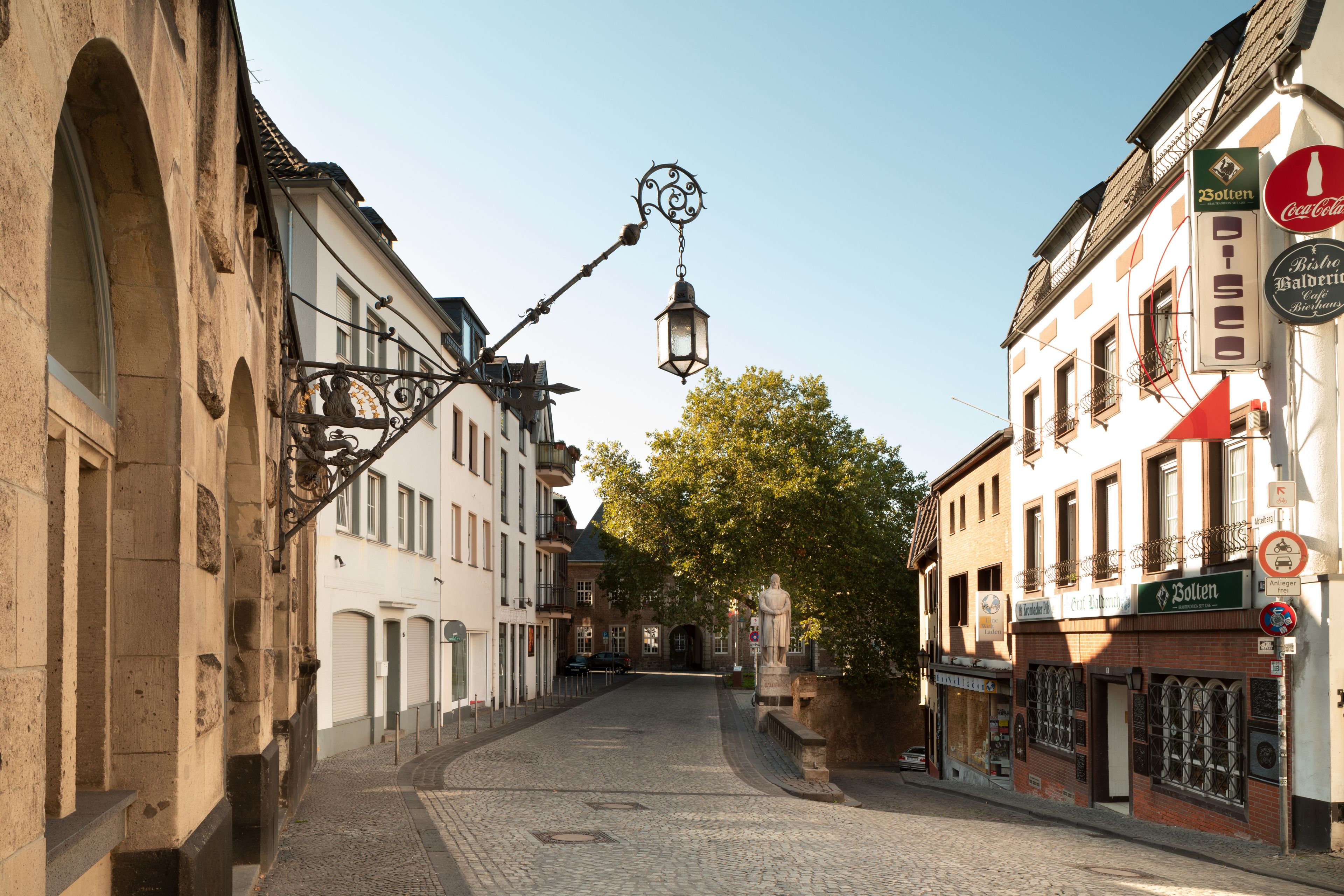 A cobblestone street with historic buildings, a street lamp, and a statue.