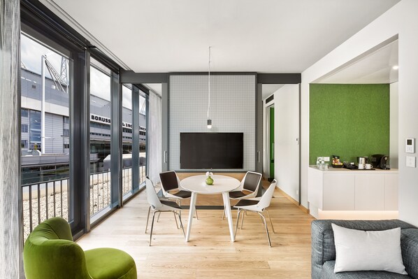 A modern living room with a round table, four chairs, a flat-screen TV, and a green accent wall.