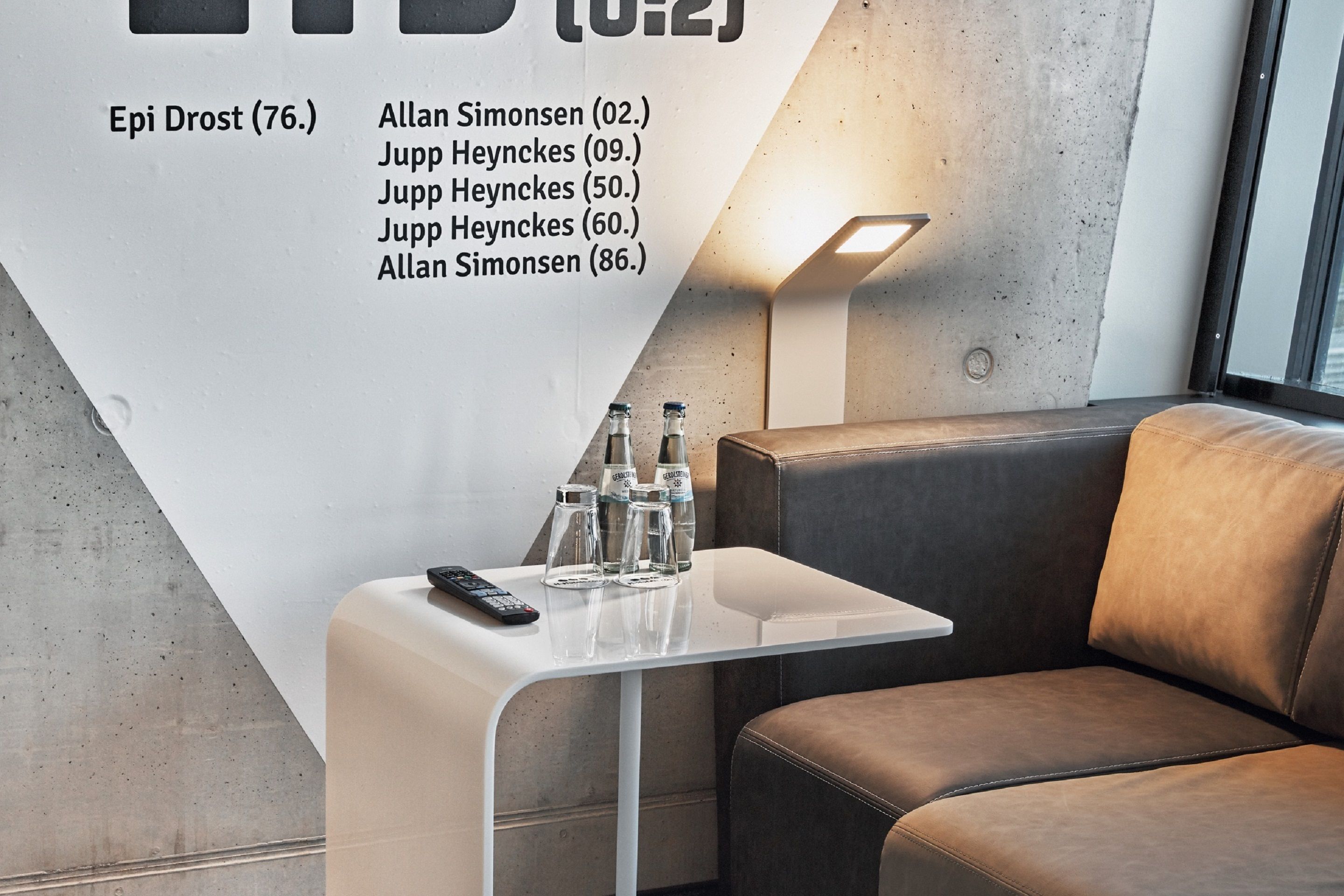 A modern lounge area with a white table, leather seating, and a wall-mounted lamp.