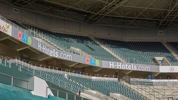 Un stade doté de plusieurs niveaux de gradins, une grande publicité pour H-Hotels.com bien visible, et un panneau indiquant la section 19A.