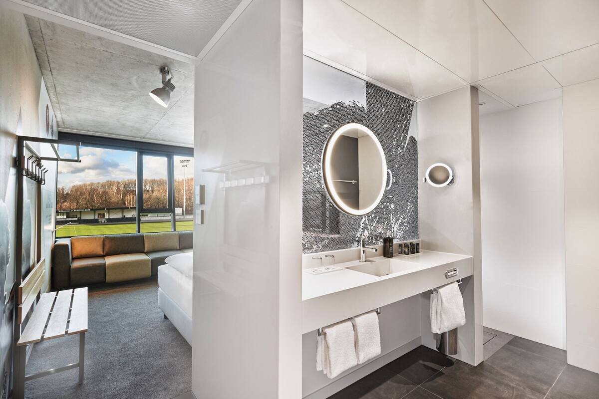 Casa de banho moderna com espelho grande, lavatório branco e suporte para toalhas.