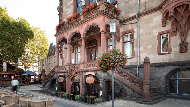 Un edificio histórico con arquitectura ornamentada, una escalera y asientos al aire libre.