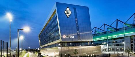 Un hôtel moderne, facilement reconnaissable grâce à son grand panneau « H4Hotel », qui se distingue par son architecture originale et un grand logo en forme de « B » sur la façade.