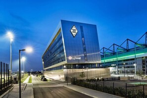 A modern hotel with a prominent 'H4Hotel' sign, featuring a unique architectural design with a large 'B' logo on the facade. - H4 Hotel Mönchengladbach im BORUSSIA-PARK (Moenchengladbach)
