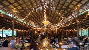 An outdoor dining area with tables set for a meal, surrounded by a wooden structure with a thatched roof, string lights, and candles. - Garden Inn Bed & Breakfast at Bee Rock (Monterey)