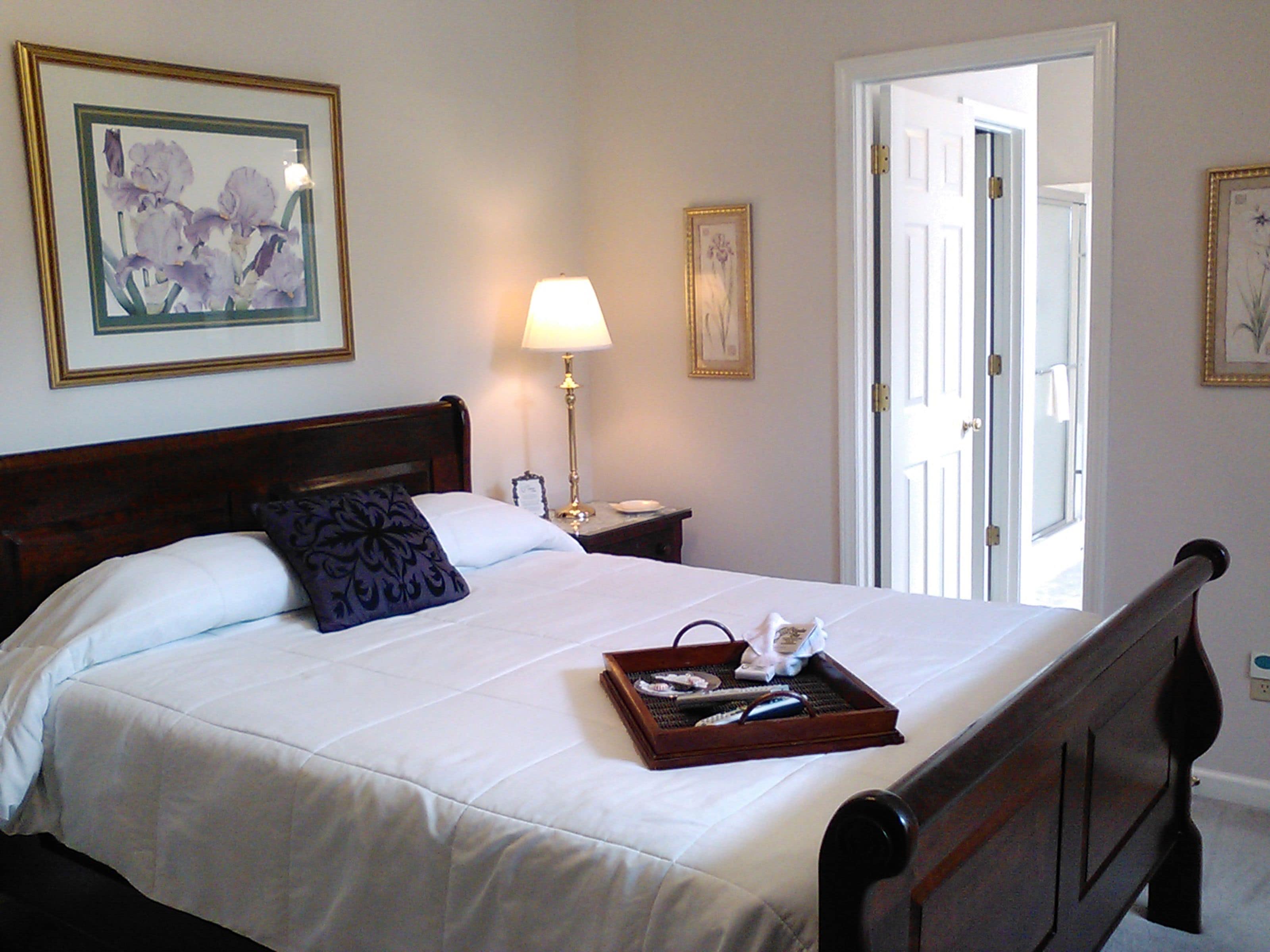A neatly made bed with a tray of toiletries, a bedside lamp, and framed artwork on the walls.