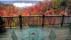 A wooden deck with a metal table and chairs, overlooking a forest with autumn foliage. - Garden Inn Bed & Breakfast at Bee Rock (Monterey)