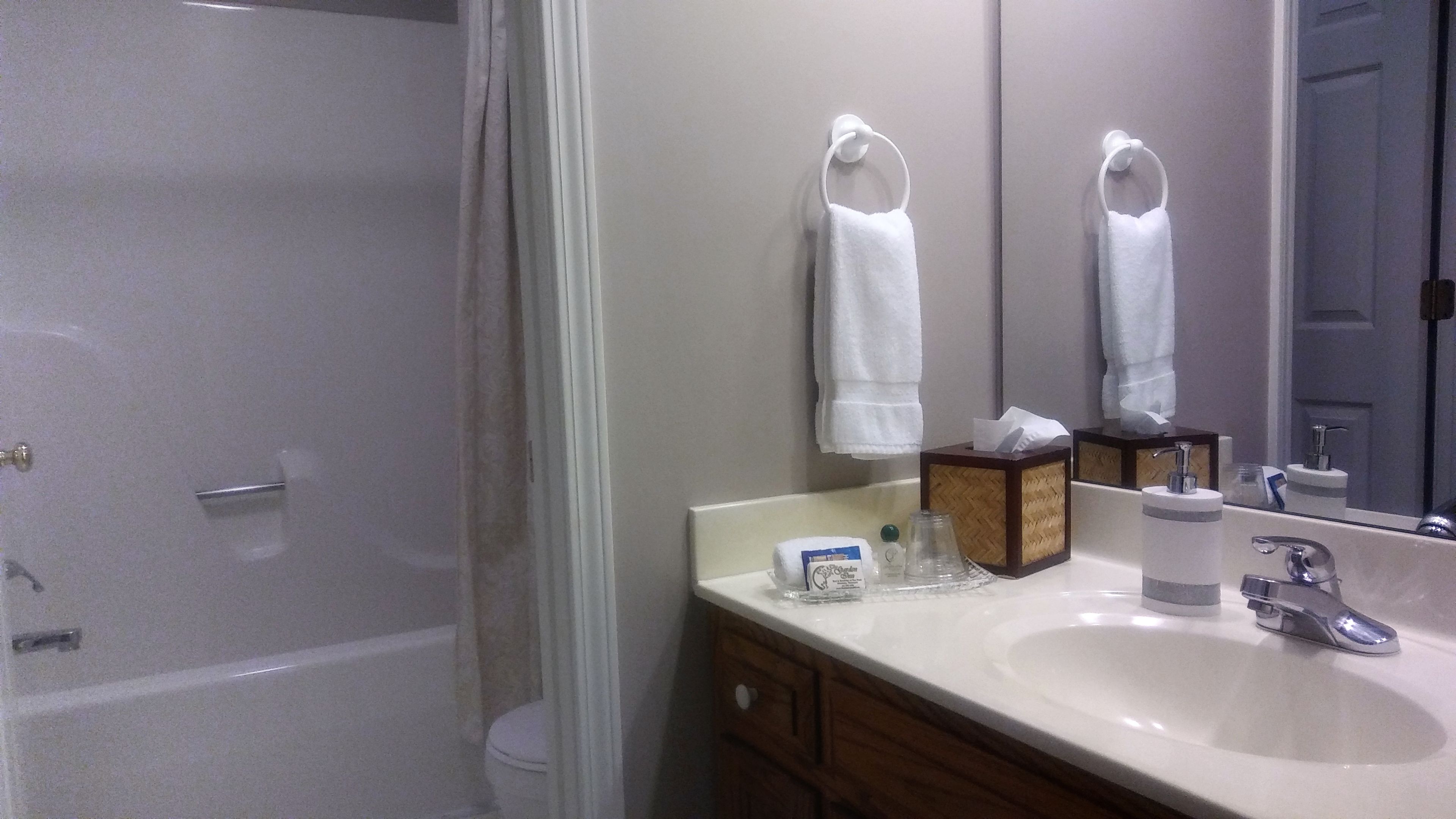 A bathroom with a bathtub, toilet, sink, and a mirror. There are two white towels hanging on hooks above the sink.
