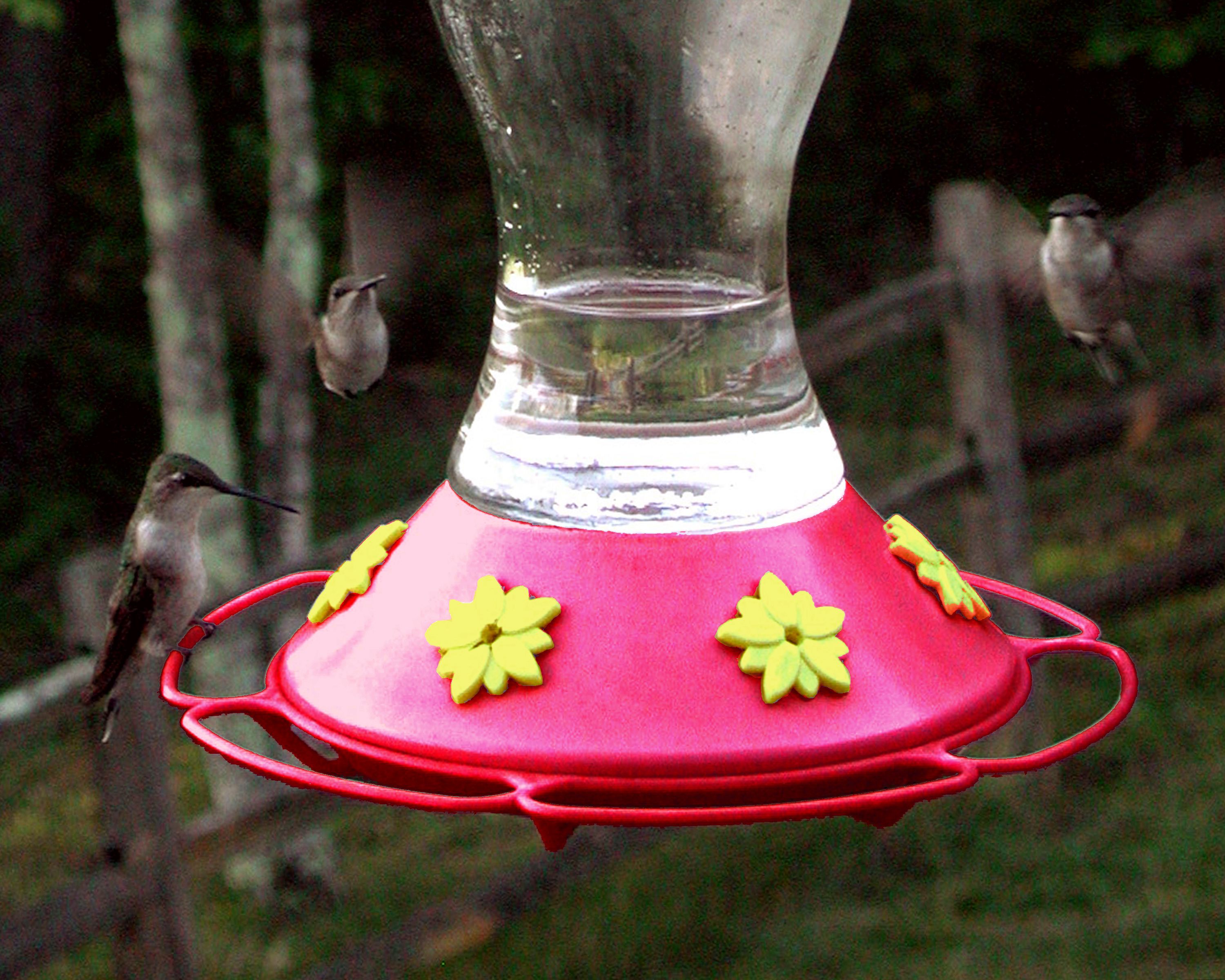 Un distributeur d’aliments pour oiseaux doté d’une base rouge et de fleurs jaunes, entouré d’arbres.