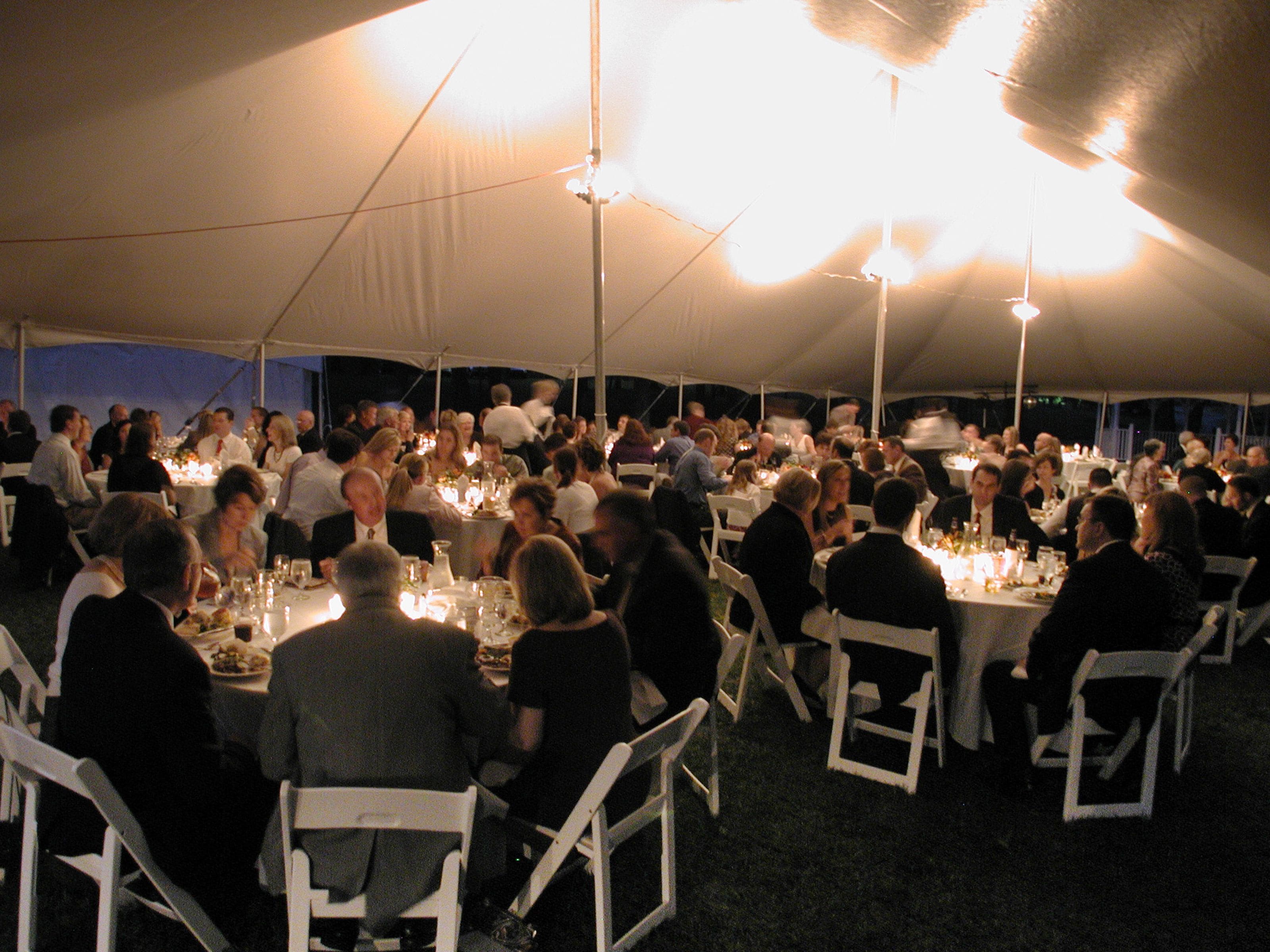 A tented dining area with round tables and white chairs, under a large canopy.