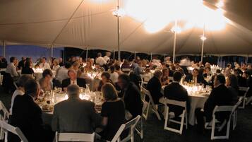 A tented dining area with round tables and white chairs, under a large canopy.