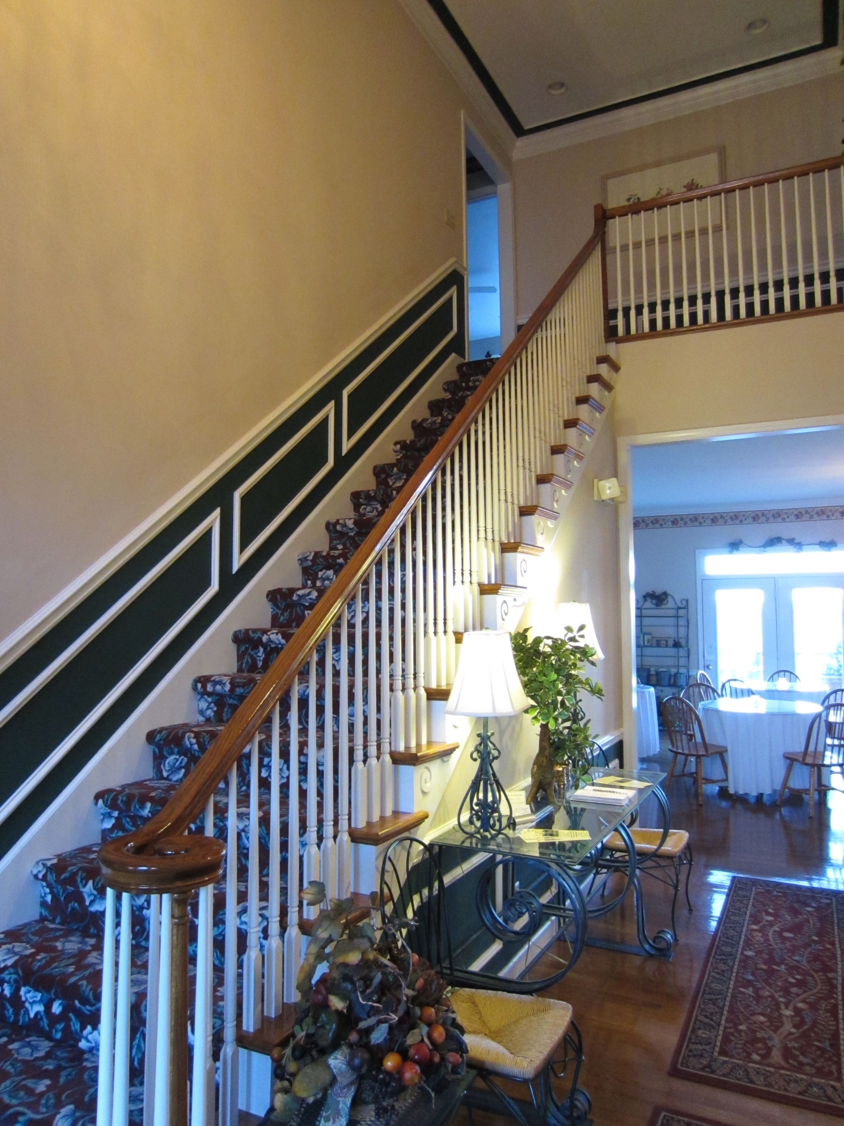 A staircase with wooden railings and floral-patterned steps, leading to a dining area with a table, chairs, and a lamp.