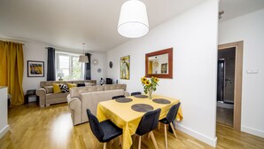 A modern living room with a dining area, featuring a sofa set, a dining table with chairs, and a large window with curtains.