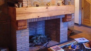 Une cheminée en pierre avec une cheminée en bois, des livres sur une table en verre et un escalier en bois à l’arrière-plan.