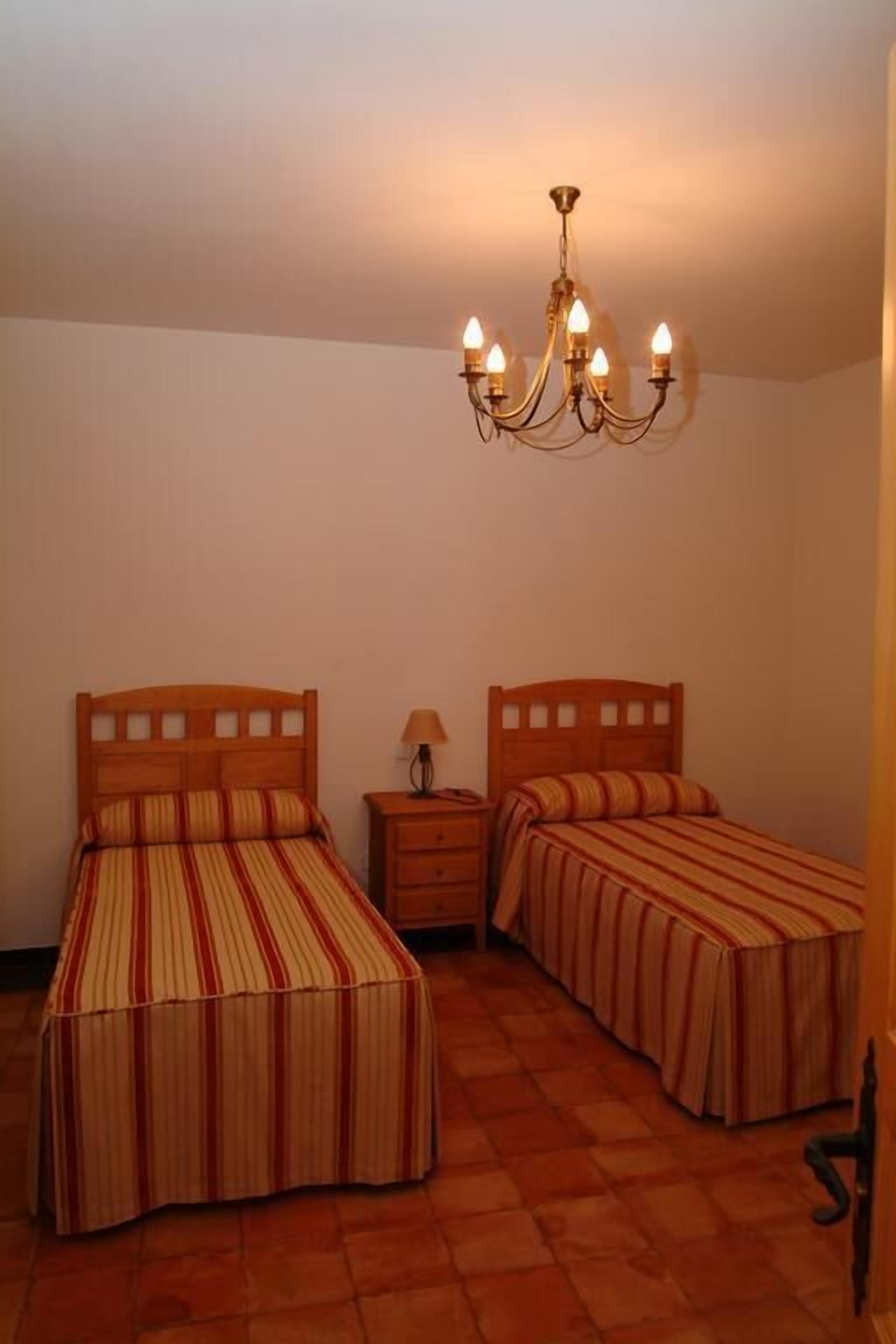 Un dormitorio con dos camas individuales, una mesita de noche, una lámpara y un candelabro.