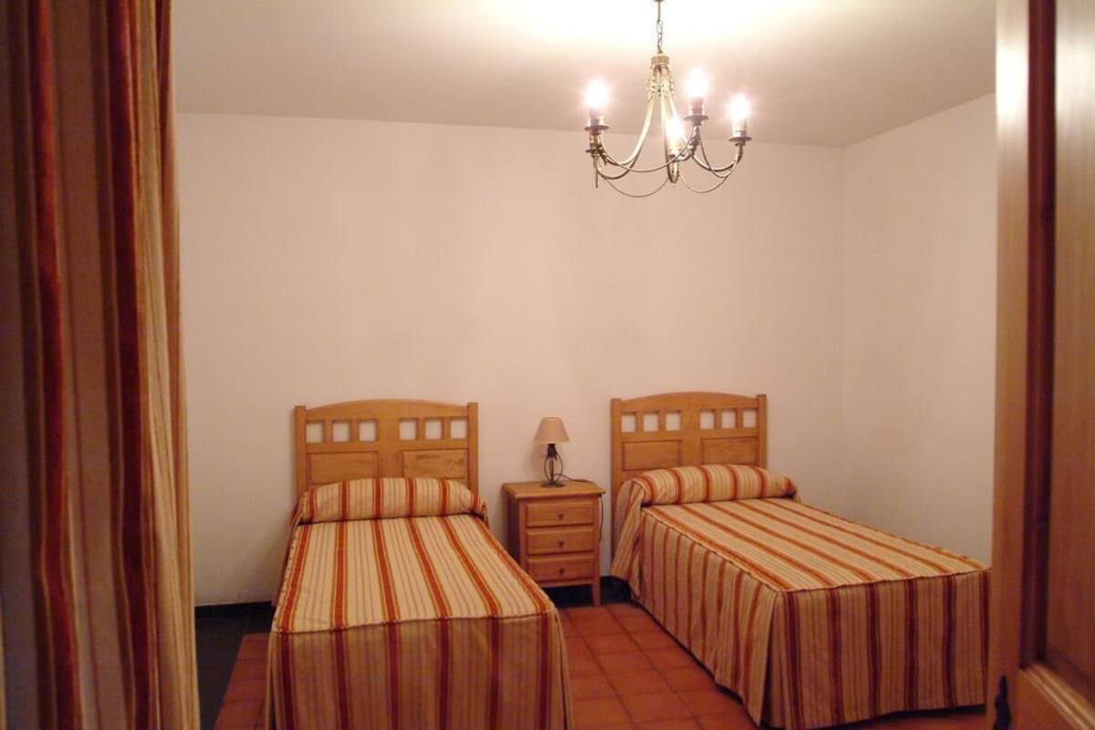 A room with two single beds, a nightstand, a lamp, and a chandelier.