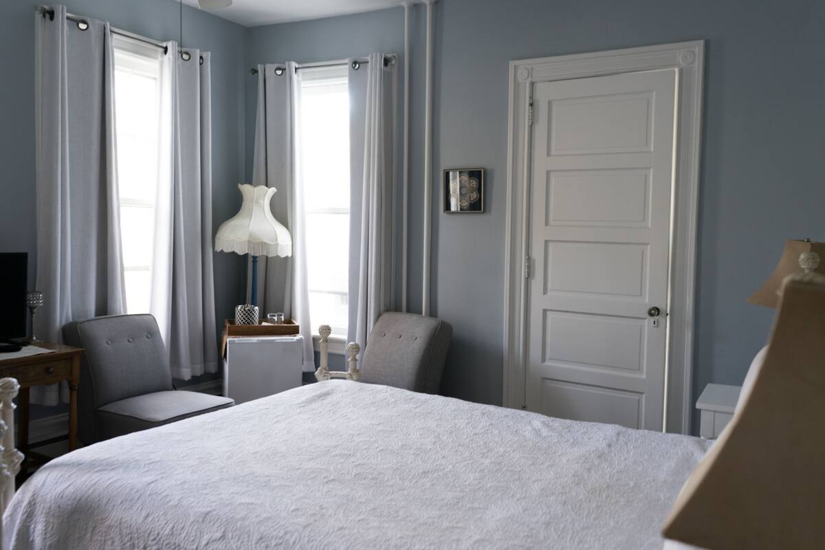 A bedroom with a bed, a chair, a desk with a lamp, and a door.