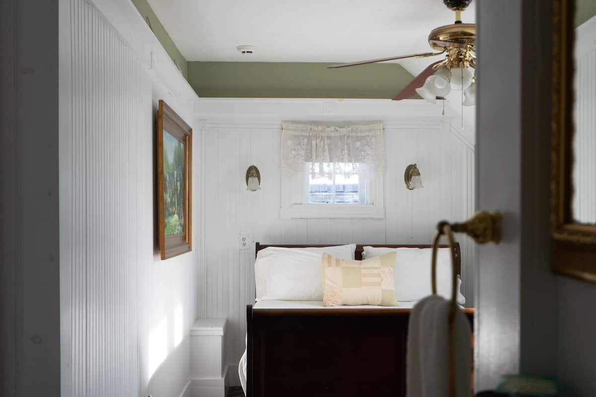 A bedroom with a bed, a window with lace curtains, a radiator, and a wooden dresser.