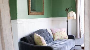 A room with a dark grey sofa, floral patterned carpet, a mirror on the wall, and a floor lamp.