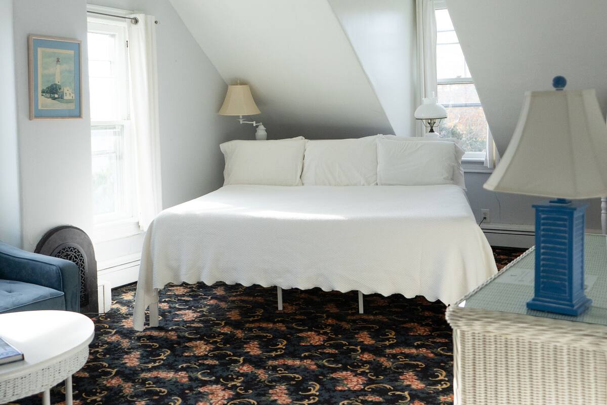 A bedroom with a bed, a ceiling fan, a lamp, and a patterned carpet.