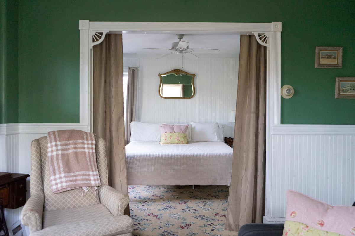 A bedroom with a bed, a chair, a ceiling fan, and a mirror on the wall.