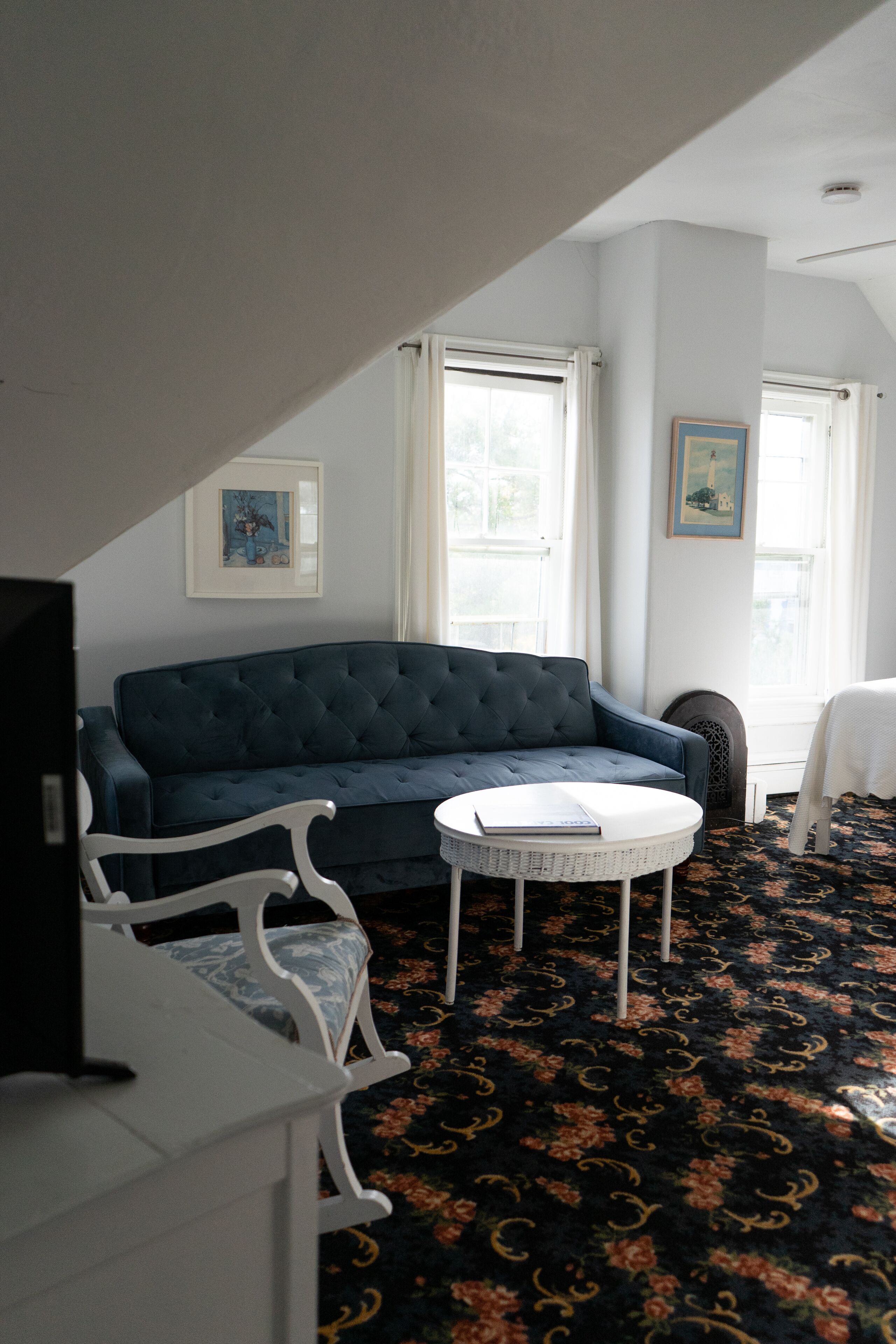 A room with a dark blue sofa, a white chair, a small white table, and a patterned carpet.