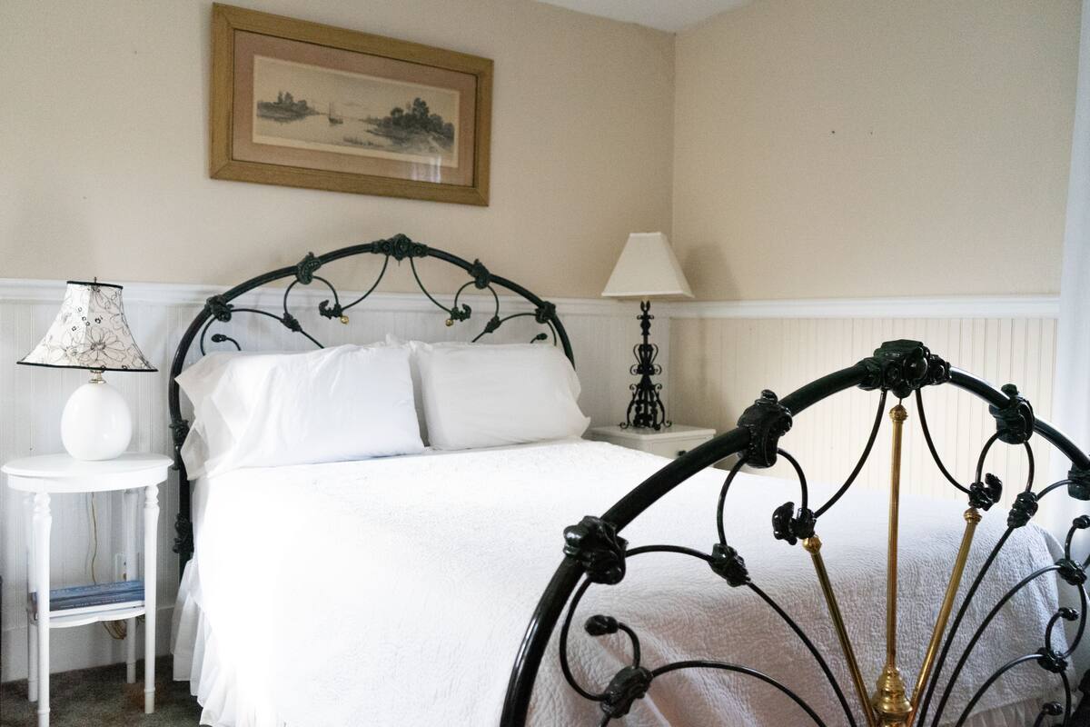 A neatly made bed with a black metal frame, a white bedside table with a lamp, and a framed picture on the wall.