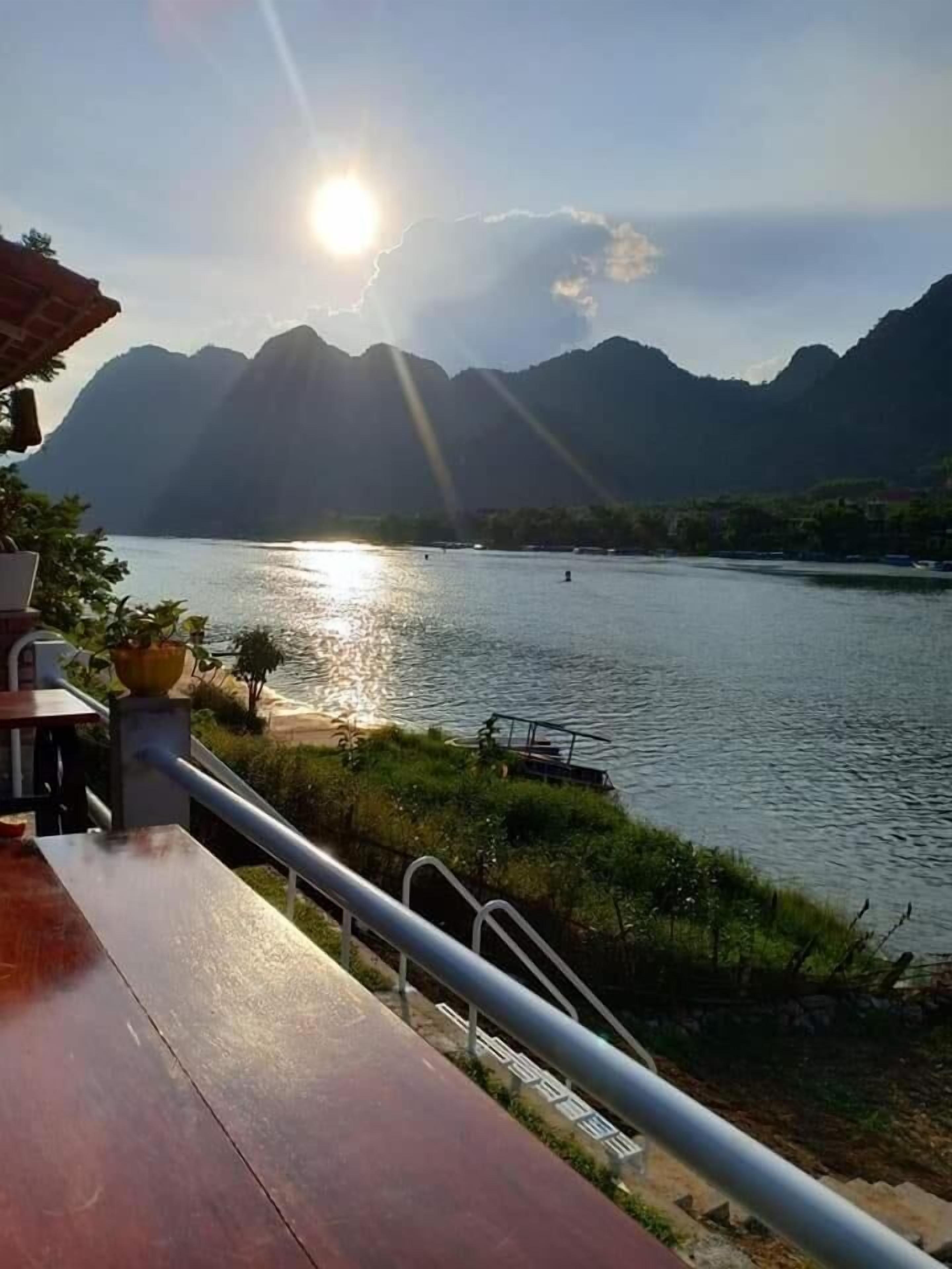 Vista de un lago con montañas al fondo, una terraza de madera y una barandilla.