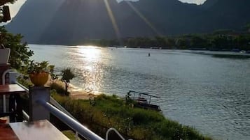 Vista de un lago con montañas al fondo, una terraza de madera y una barandilla.